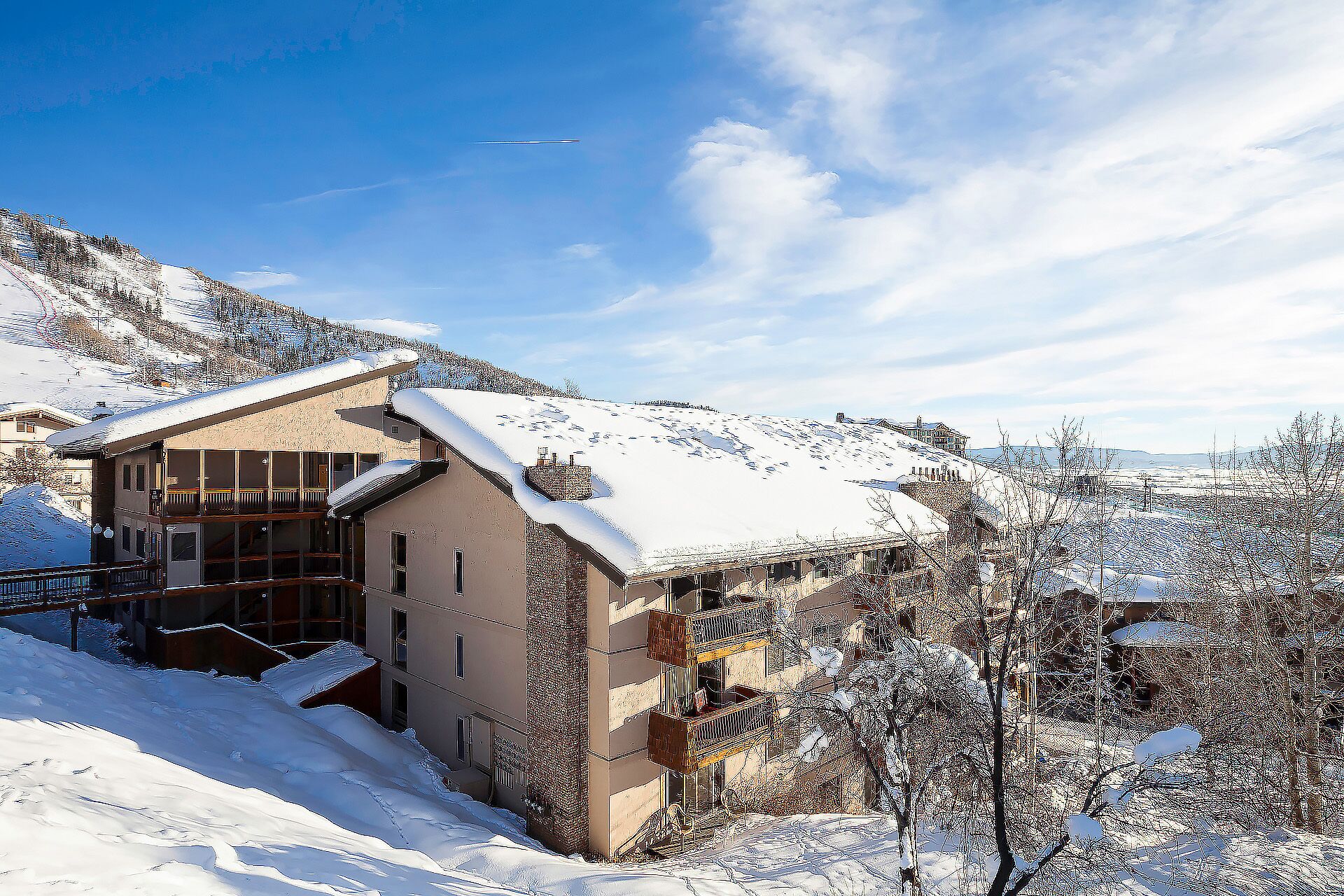 A snow-covered building with multiple balconies, a ski slope in the background, and a clear sky.