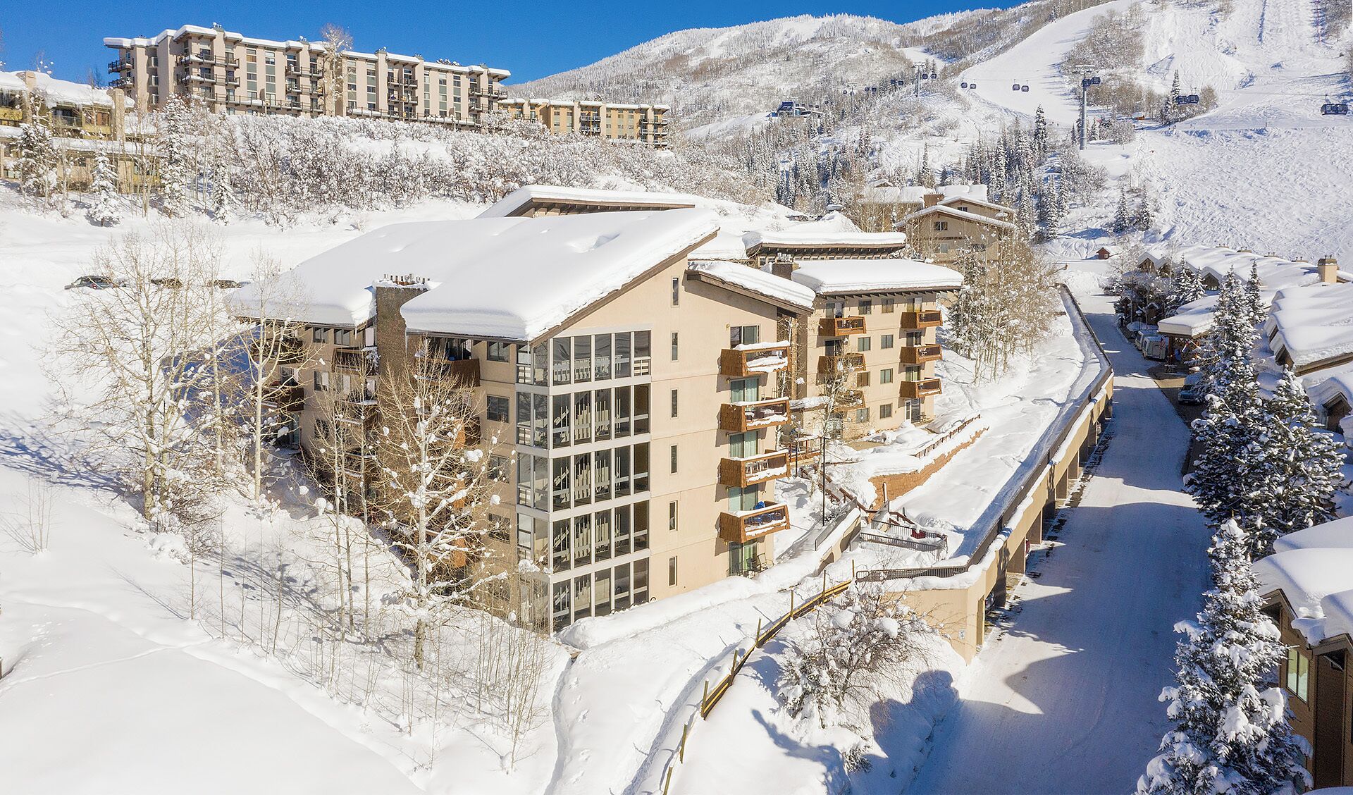 A snow-covered resort with multiple buildings, including a prominent glass-fronted structure with balconies.