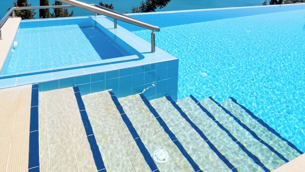 Un ciel d’un bleu éclatant, une piscine avec vue sur la mer et des marches menant à la piscine.