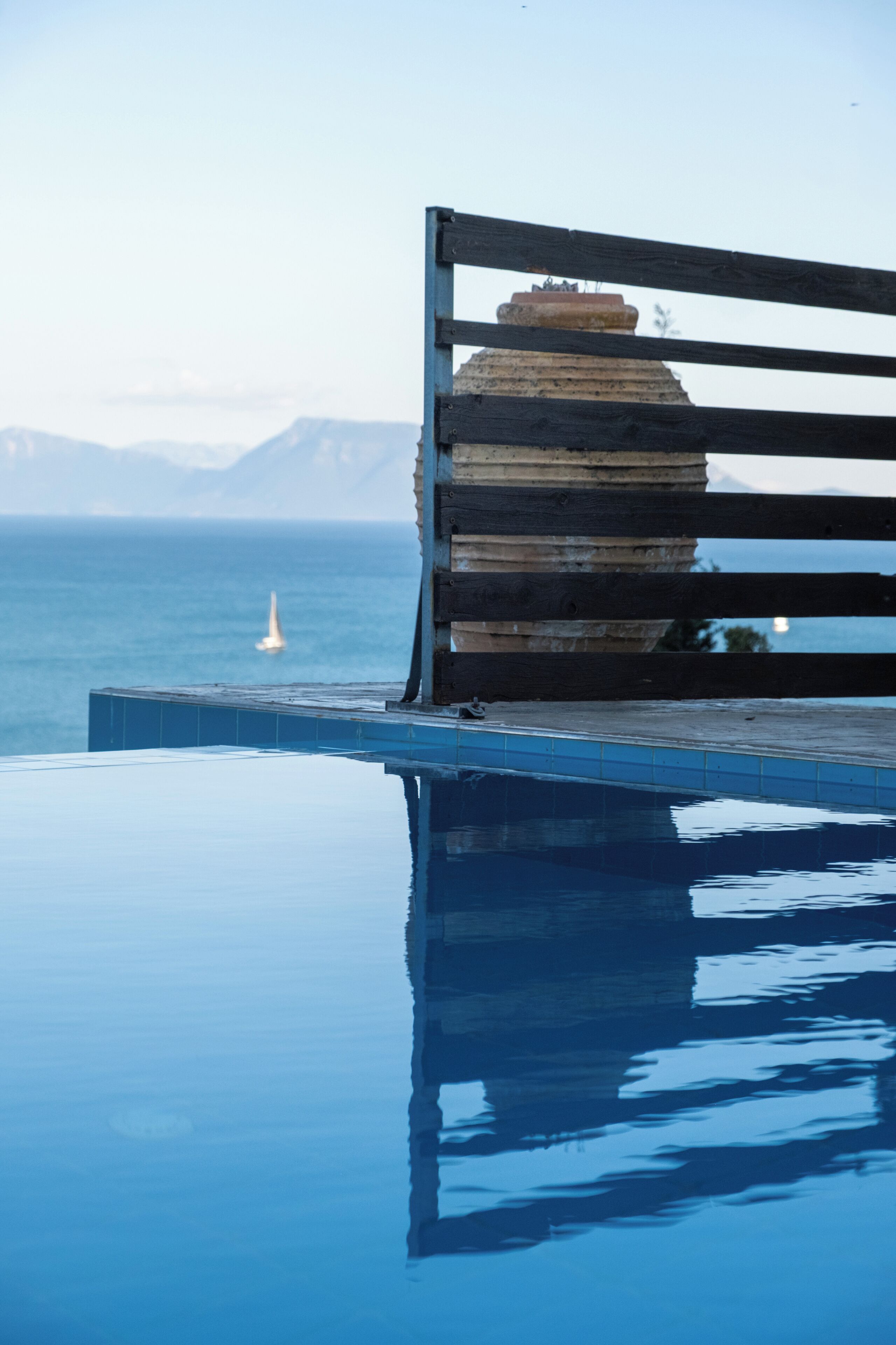 Une piscine avec un banc en bois et une vue sur la mer et les montagnes.