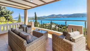 Un balcon agrémenté de meubles en osier, d’une table en verre et offrant une vue sur un lac et des montagnes.