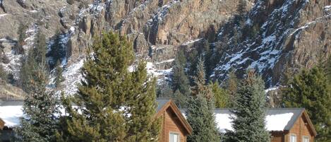 A cabin with a wooden exterior, surrounded by snow-covered ground and trees, with a mountainous backdrop.