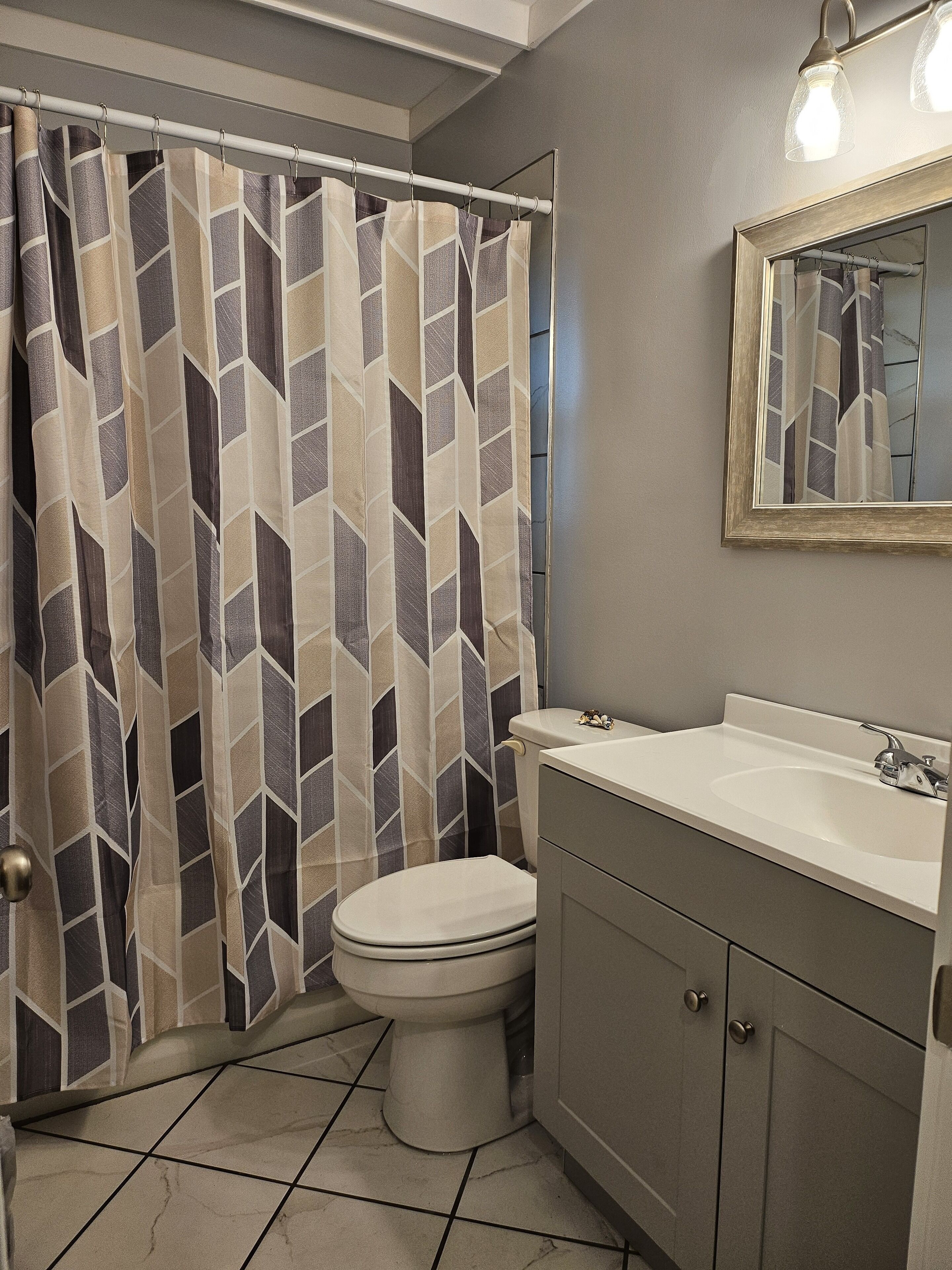 A bathroom with a shower curtain, toilet, sink, and cabinet.