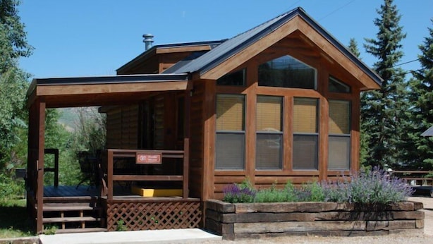 Une cabane en bois dotée d’un porche abrité et de grandes fenêtres.