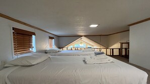 Une chambre avec deux lits, un plafond en pente et une vue sur l’extérieur.