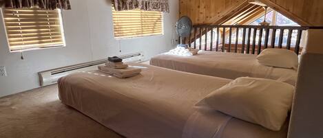 A room with two beds, a ceiling fan, and a view of a wooden staircase.