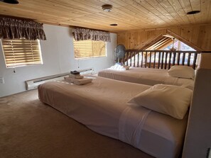 Ein Zimmer mit zwei Betten, einem Deckenventilator und Blick auf eine Holztreppe.