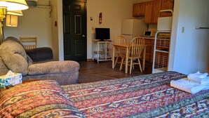 A cozy room with a bed, a chair, a desk with a computer, and a kitchenette. - Hotel Style Lodge Room w/Kitchenette (Almont)