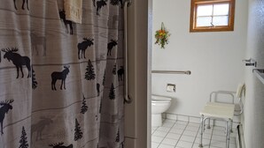 A bathroom with a white toilet, a handrail, a small window, and a shower curtain with moose and tree patterns. - Hotel Style Lodge Room w/Kitchenette (Almont)