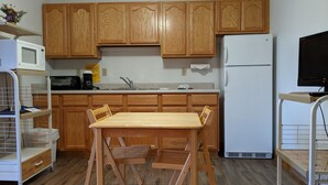 A compact kitchen with wooden cabinets, a white refrigerator, a microwave, and a small dining table with chairs. - Hotel Style Lodge Room w/Kitchenette (Almont)