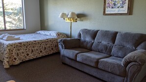 A room with a bed and a sofa, a lamp, and a framed picture on the wall. - Hotel Style Lodge Room w/Kitchenette (Almont)