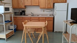 A compact kitchen with wooden cabinets, a microwave, a coffee maker, a sink, and a small table with chairs. - Hotel Style Lodge Room w/Kitchenette (Almont)
