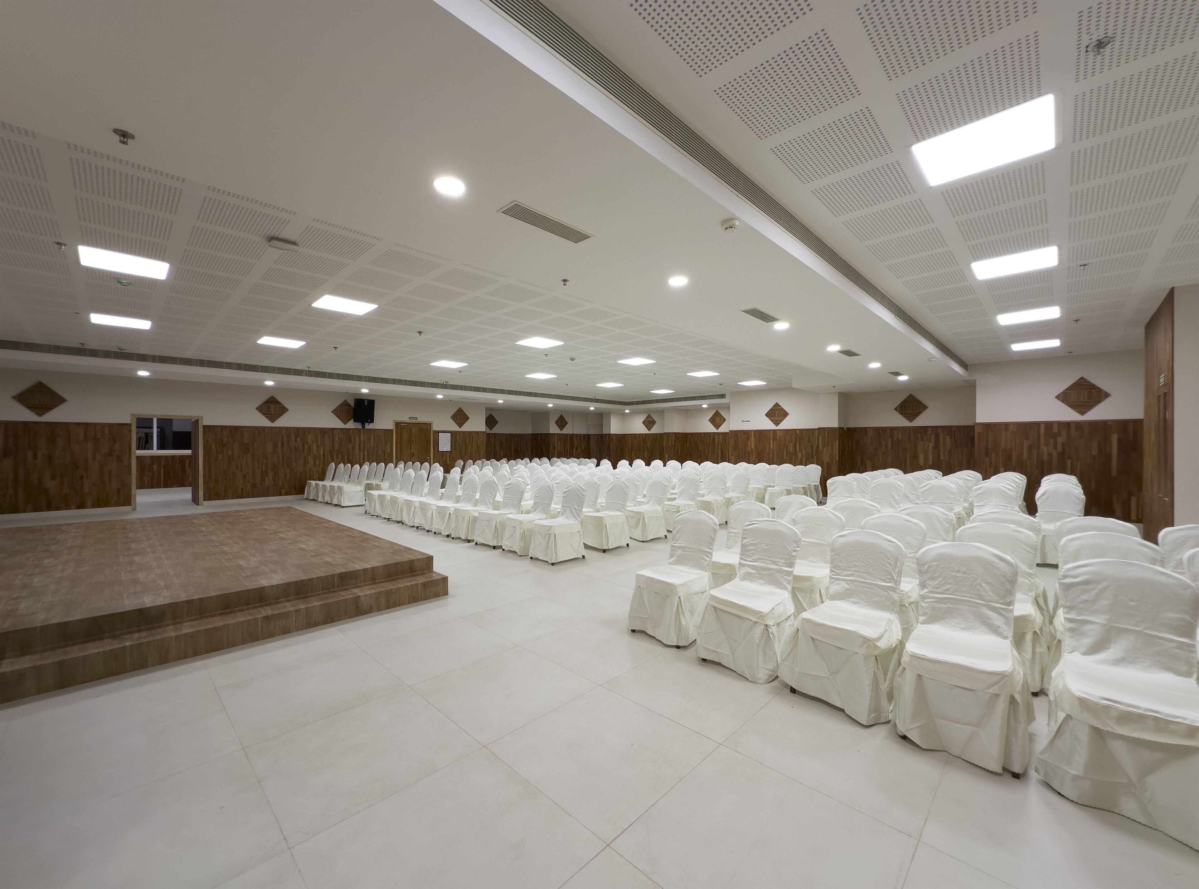 A large, well-lit conference room with rows of white chairs and a stage area.