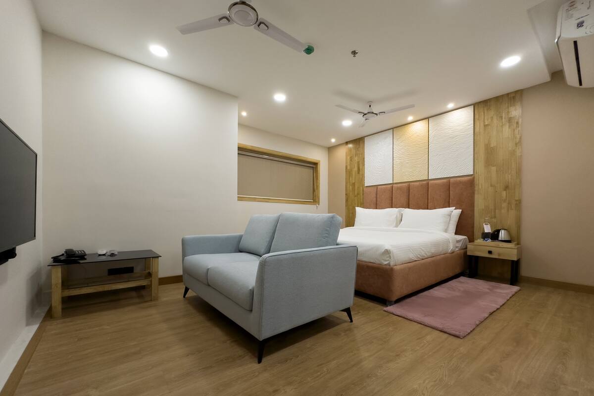 A modern bedroom with a bed, a sofa, a small table, and a TV.