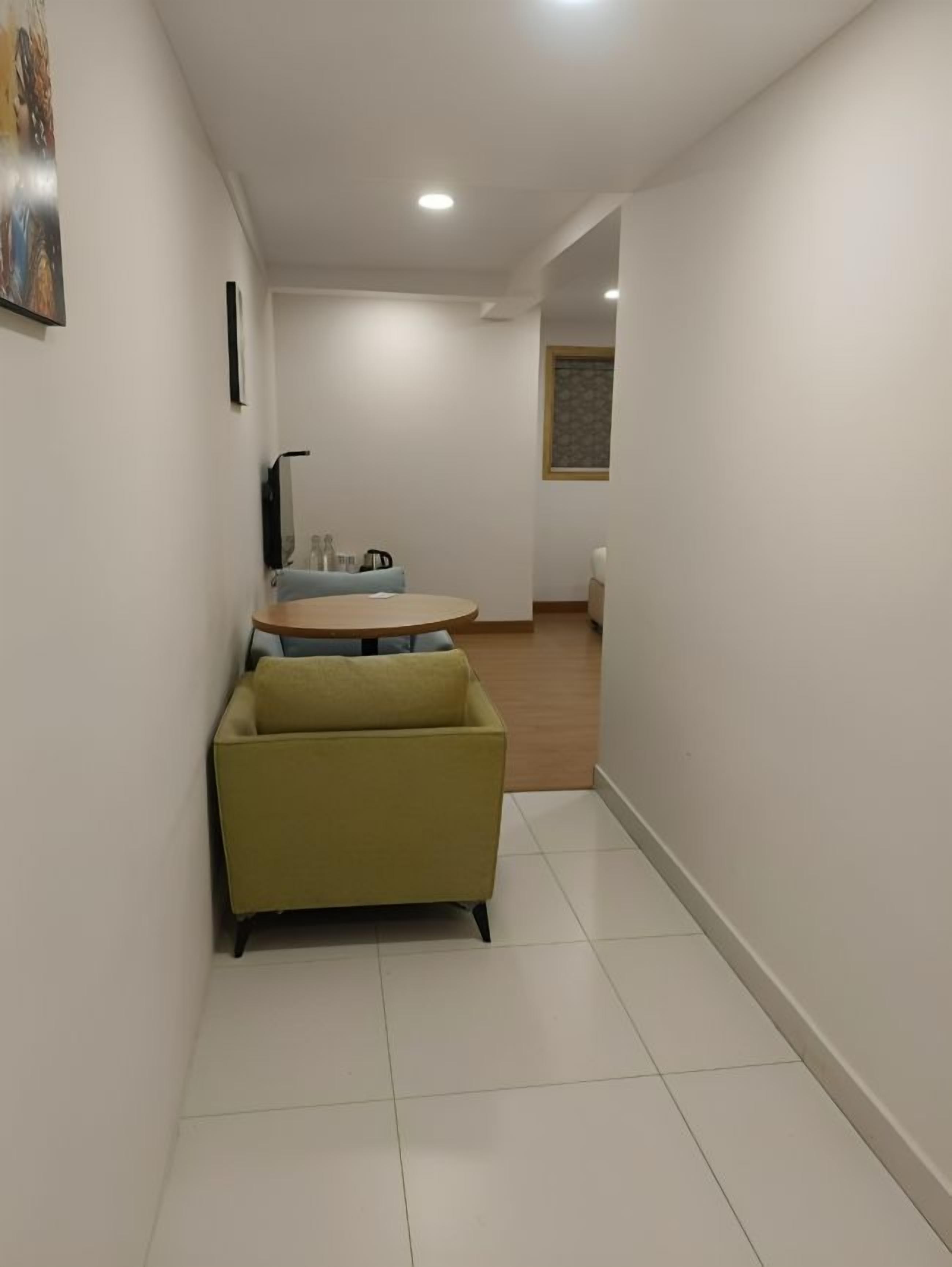 A hallway with a yellow sofa, a round table with chairs, and a small kitchen area in the background.