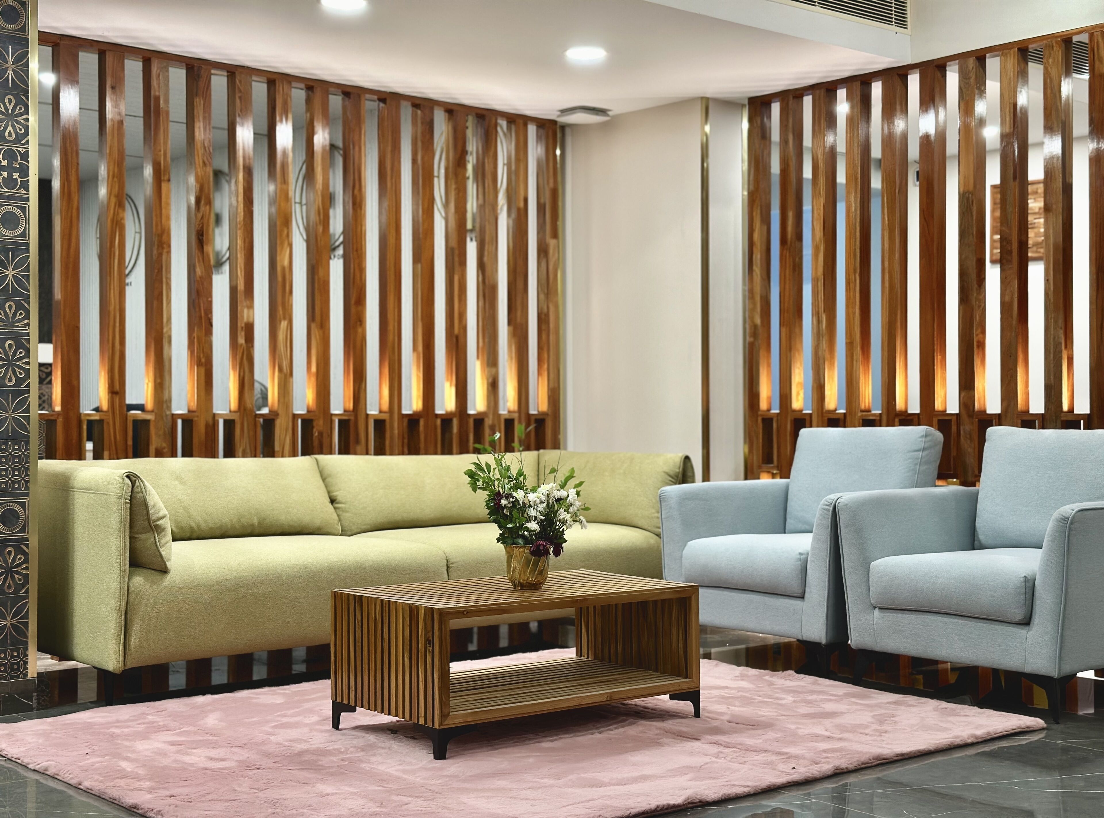 A modern living room with a green sofa, a light blue armchair, and a wooden coffee table with a vase of flowers.