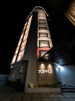 Un edificio moderno con fachada curva, ventanas iluminadas y un letrero que dice '7APPLE'.