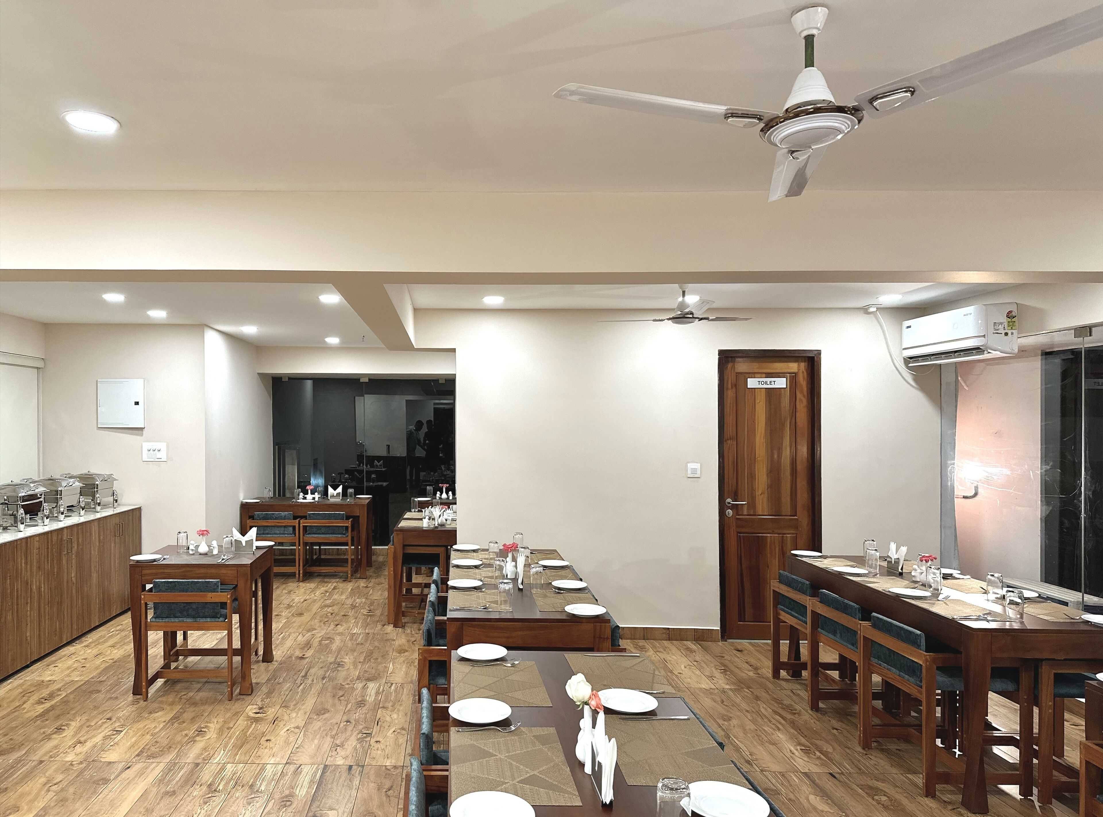 A dining area with wooden tables and chairs, a ceiling fan, and an air conditioning unit.