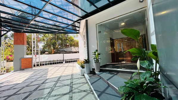 A modern building entrance with a glass door, potted plants, and a tiled patio area. - 7 Apple Hotel Guruvayur, Kerala (Chavakkad)