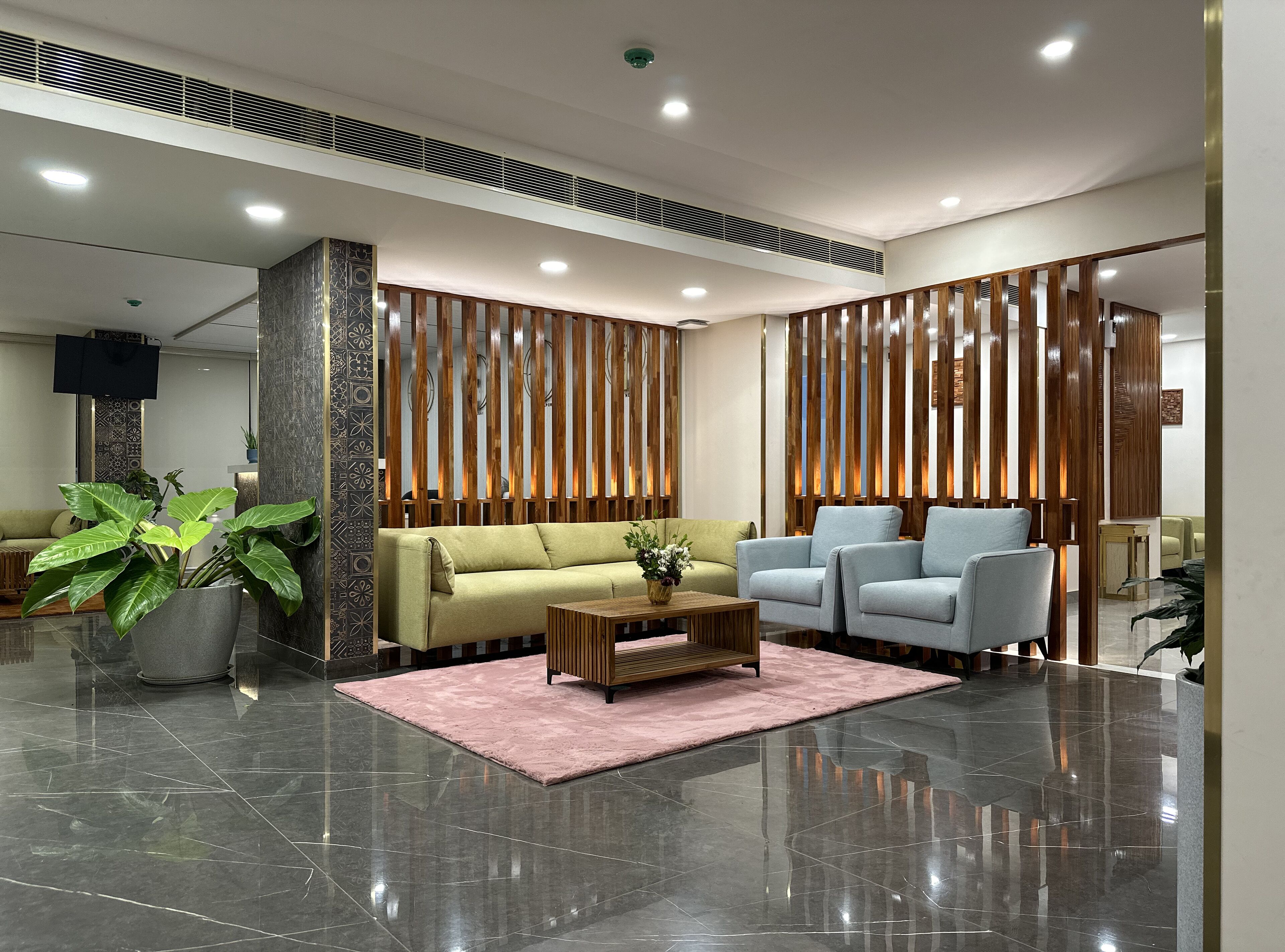 A modern lobby with a sofa, two armchairs, a coffee table, and a large potted plant.