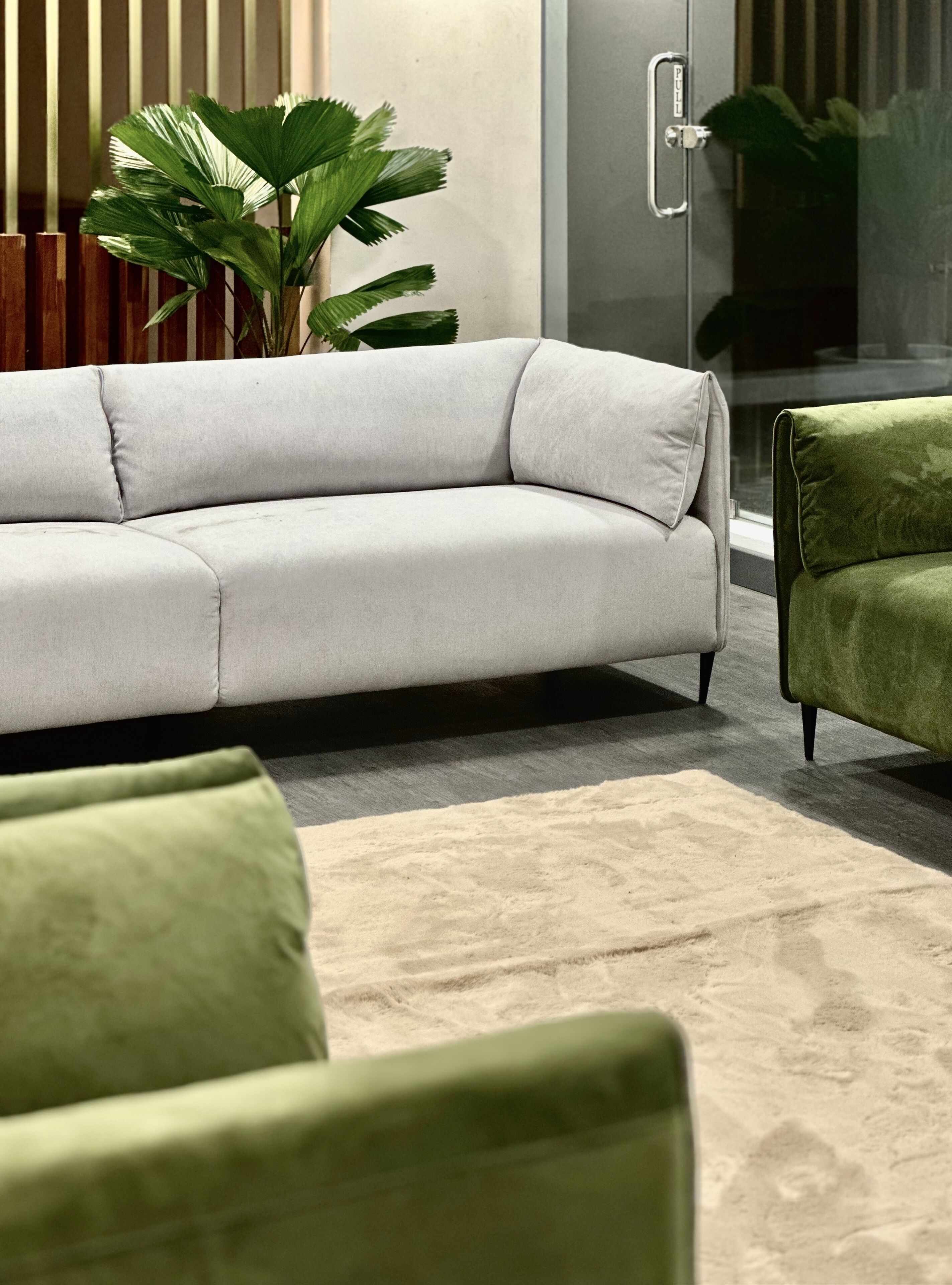 Una sala moderna con un sofá gris, un sillón verde y una planta grande en maceta.
