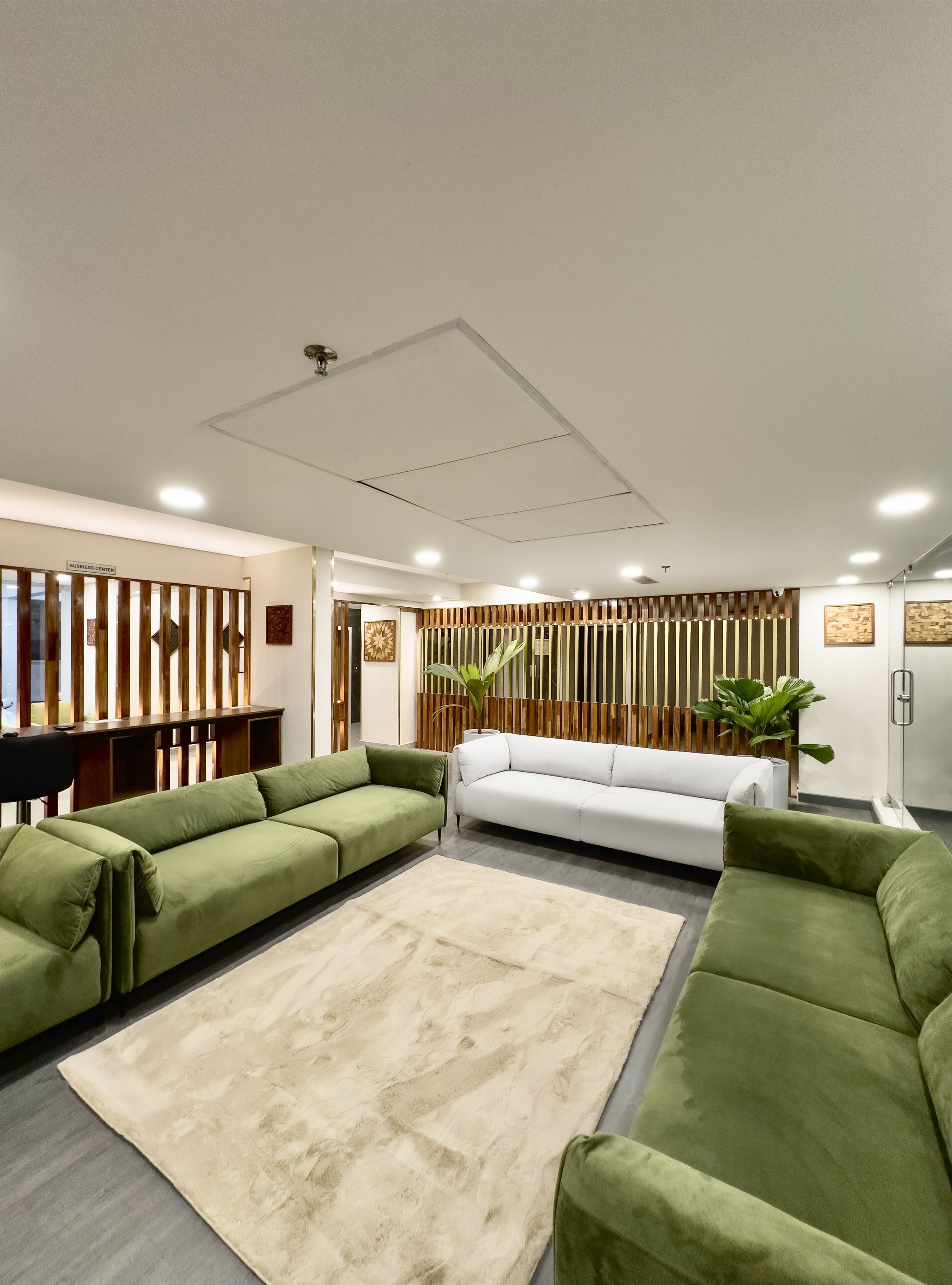 Una sala de estar moderna con sofás verdes, alfombra color beige y paneles de madera.