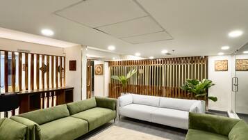 A modern living room with green sofas, a beige rug, and wooden partitions.