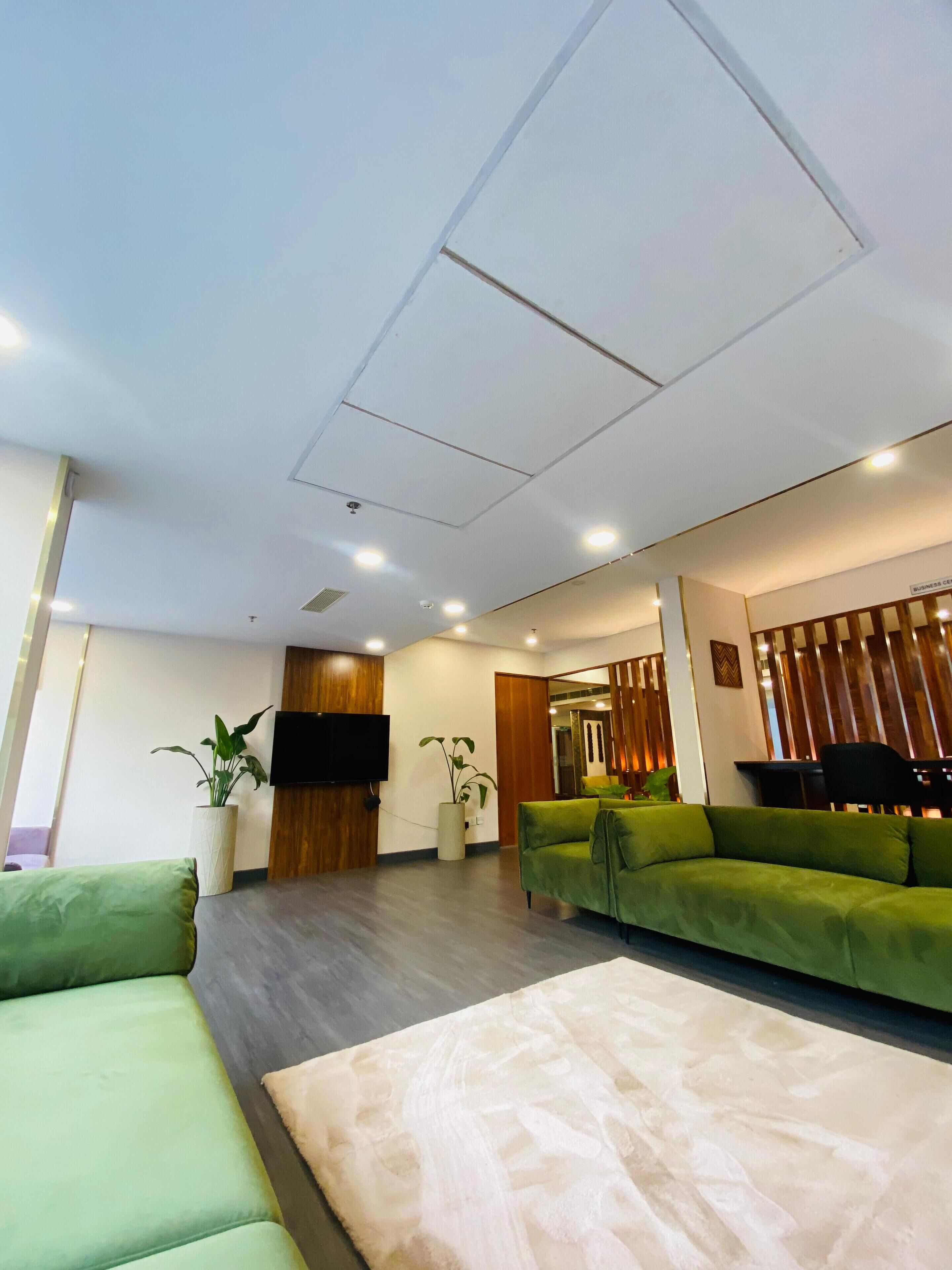 A modern living room with green sofas, a flat-screen TV, and a wooden accent wall.