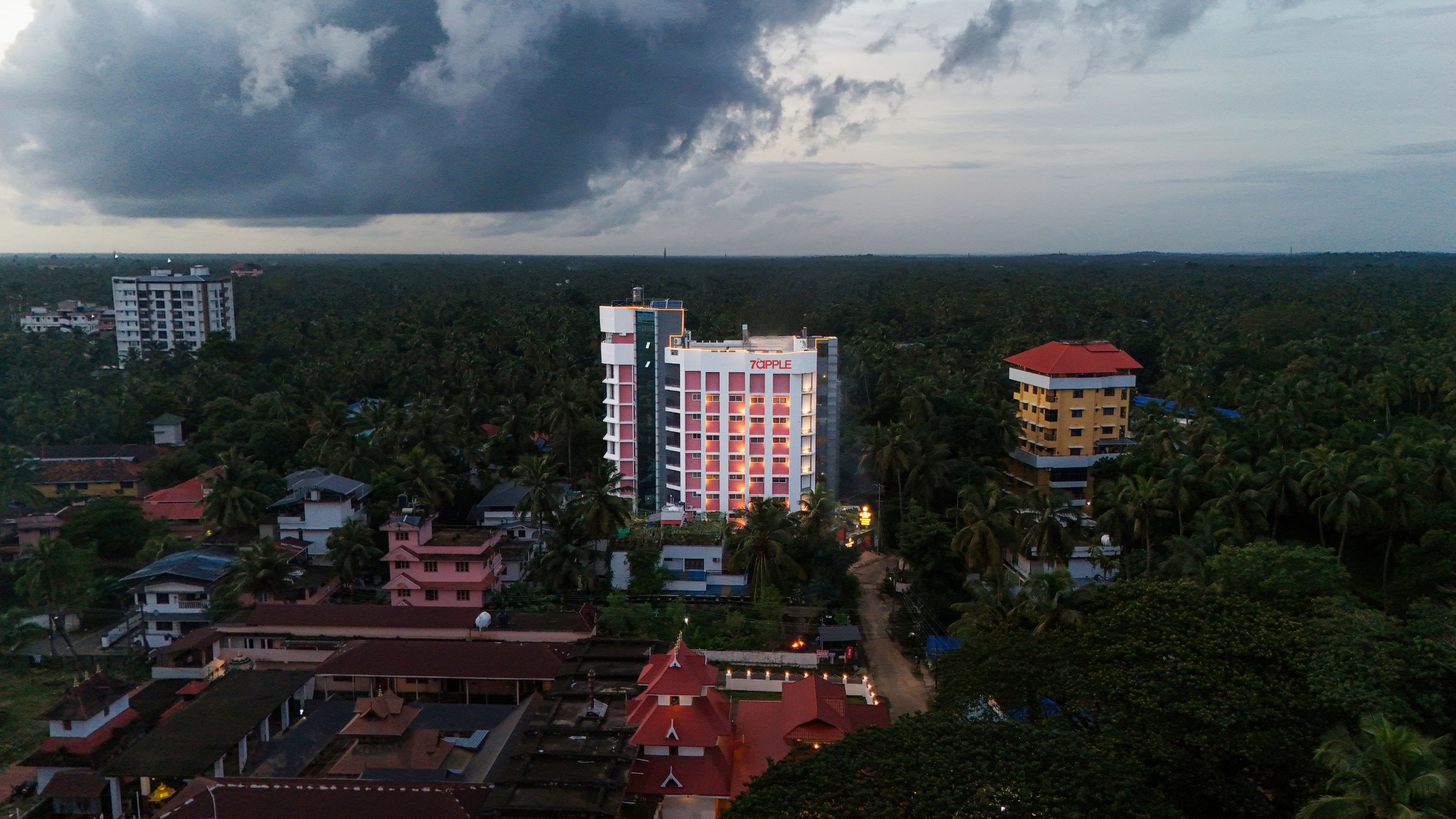 A hotel with multiple floors, surrounded by dense vegetation and other buildings.