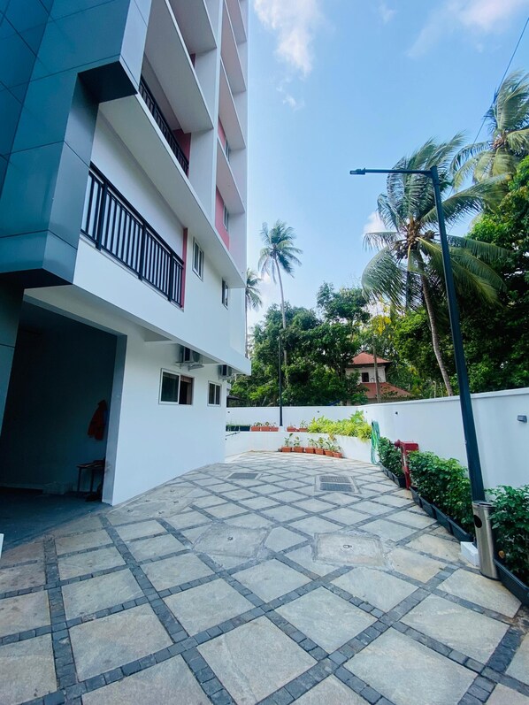 A modern building with a tiled courtyard, balconies, and surrounding greenery. - 7 Apple Hotel Guruvayur, Kerala (Chavakkad)