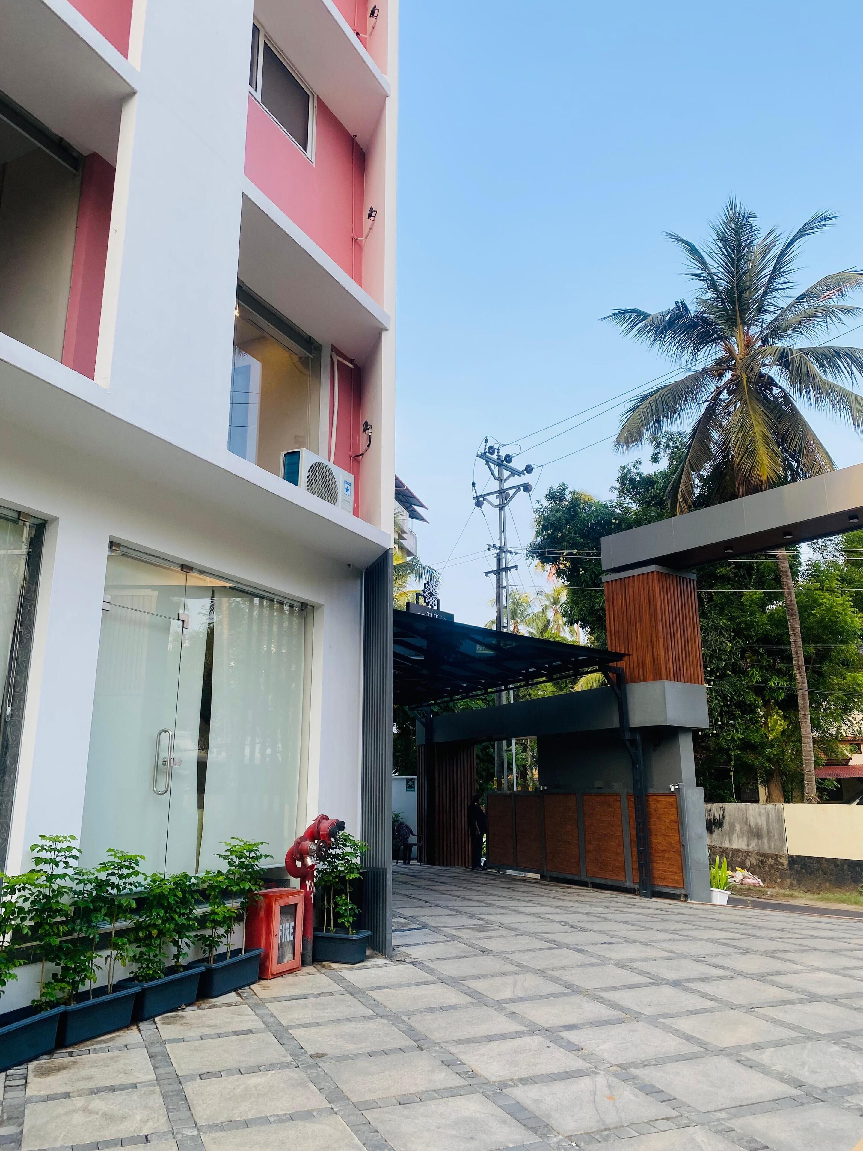 A modern building with a glass entrance, a covered outdoor area, and a palm tree in the background.