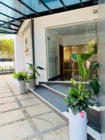 Una entrada de edificio moderna con puerta de vidrio, una escalera que sube y plantas en macetas.