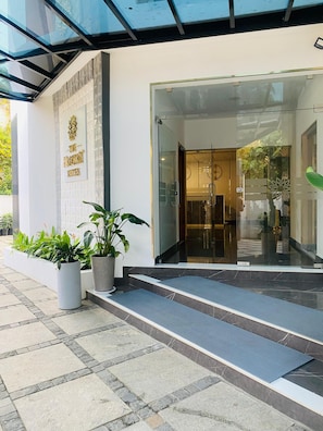 A hotel entrance with a glass door, a sign reading "The Elegant Suites", and a potted plant in front. - 7 Apple Hotel Guruvayur, Kerala (Chavakkad)