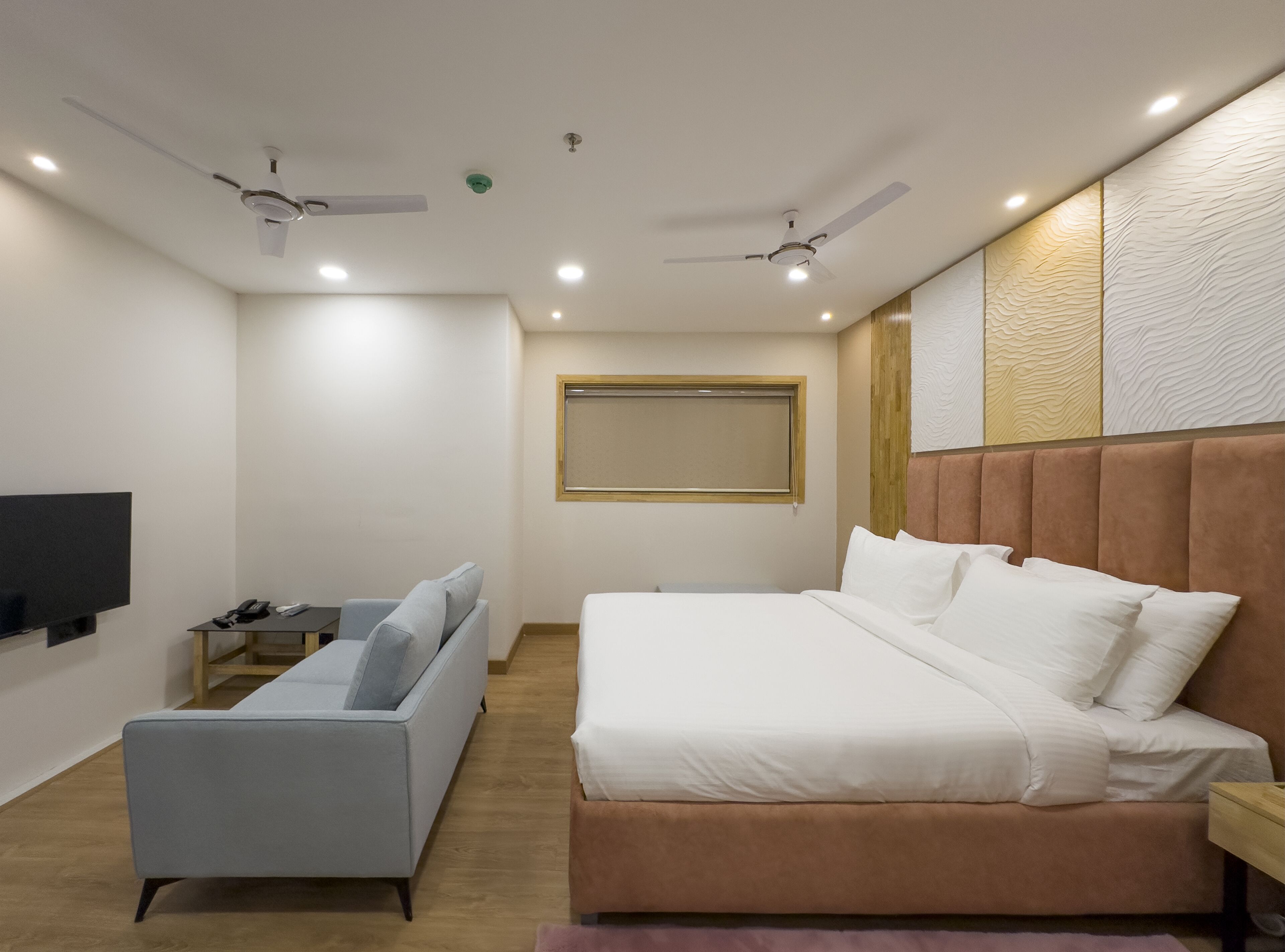 A modern bedroom with a bed, a sofa, a TV, and two ceiling fans.