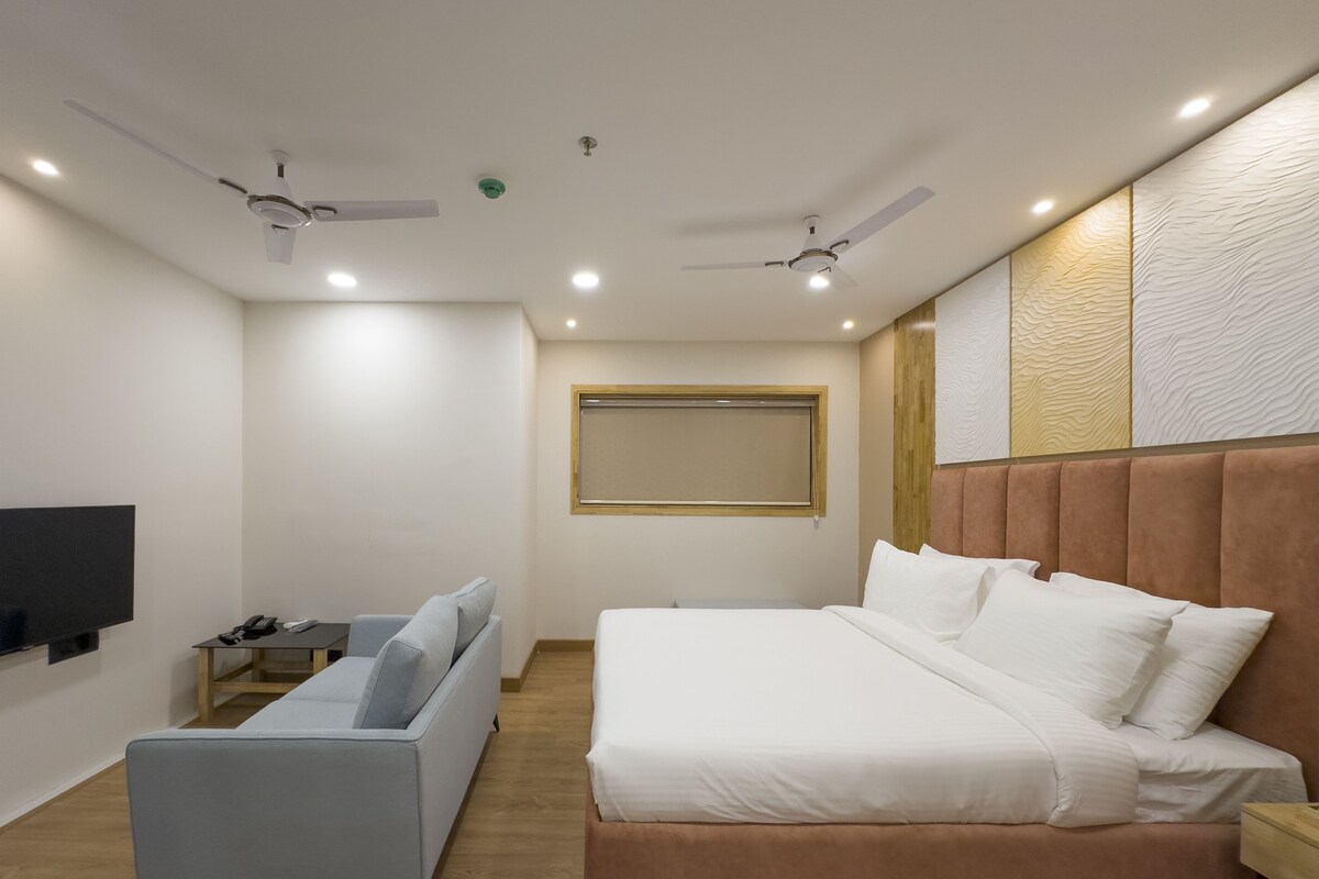 A modern bedroom with a bed, a sofa, a TV, and two ceiling fans.