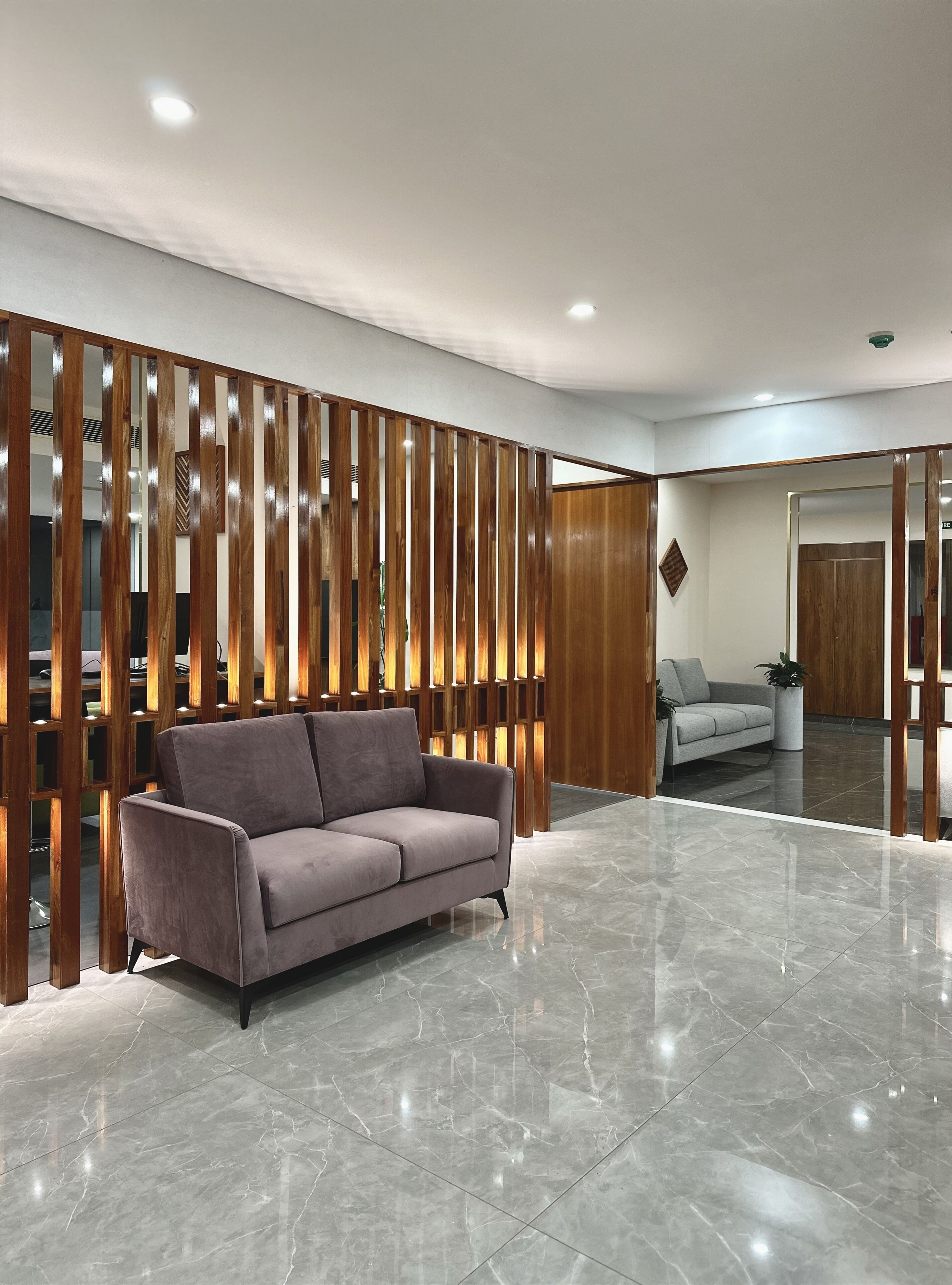 A modern lobby with a grey sofa, a wooden partition, and a marble floor.
