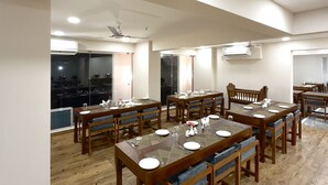 Un espace repas comprenant plusieurs tables et chaises en bois, des spots encastrés au plafond et des unités de climatisation.