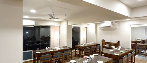 Comedor con varias mesas y sillas de madera, luces empotradas en el techo y unidades de aire acondicionado.