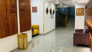 Un hall d’hôtel doté d’un sol en marbre poli, de lambris en bois sur les murs et d’un escalier menant aux étages supérieurs.