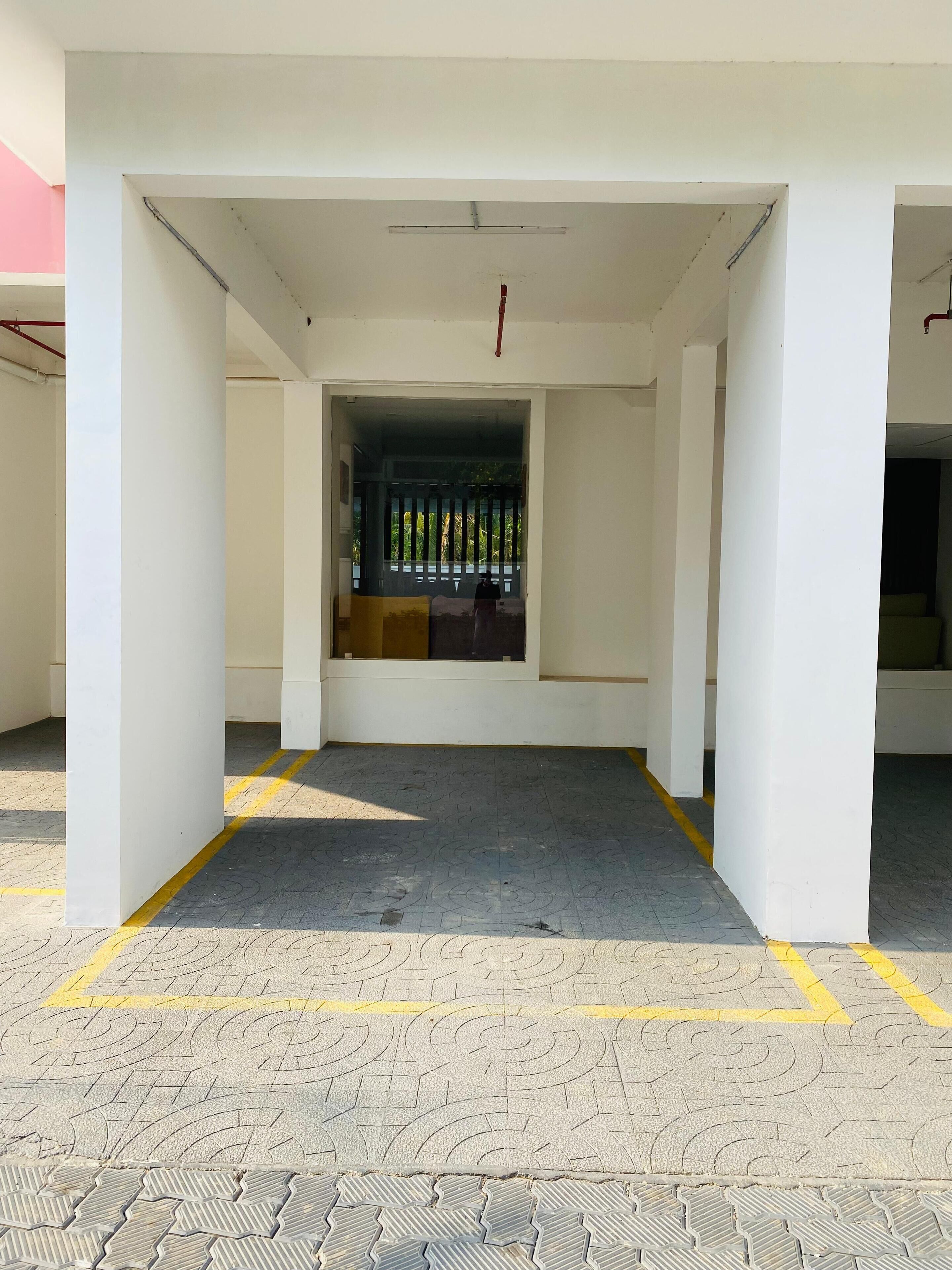 A covered outdoor area with a central entrance, white pillars, and a tiled floor with yellow lines.
