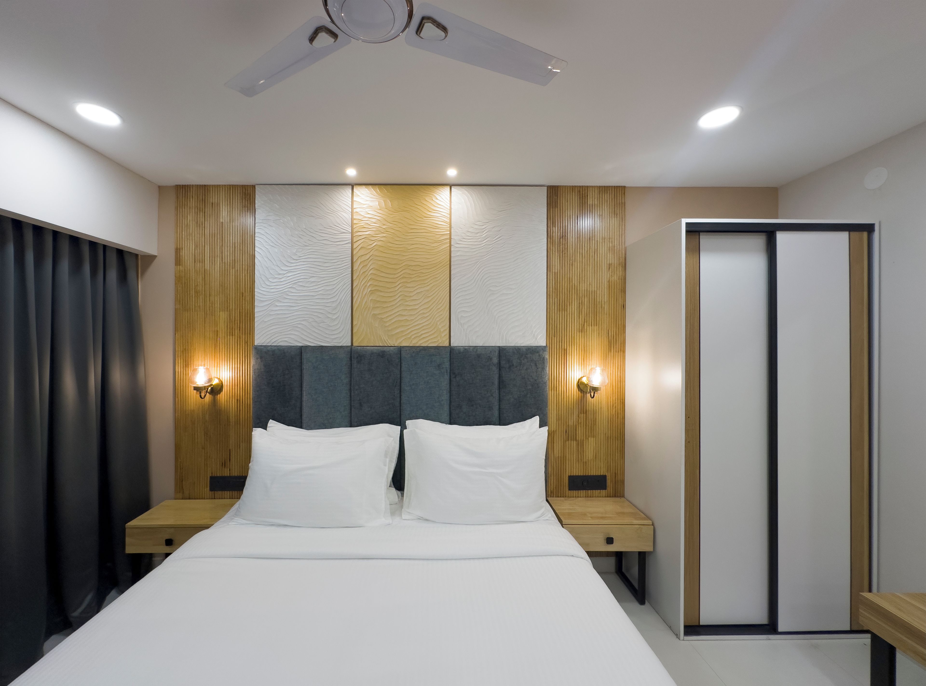 Une chambre d’hôtel moderne équipée d’un lit, de tables de chevet, d’une armoire et d’un ventilateur de plafond.