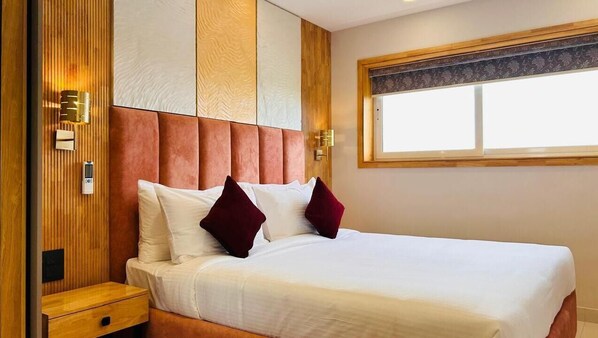 A hotel room with a large bed, wooden paneling on the walls, a nightstand, and a window with a view. - 7 Apple Hotel Guruvayur, Kerala (Chavakkad)