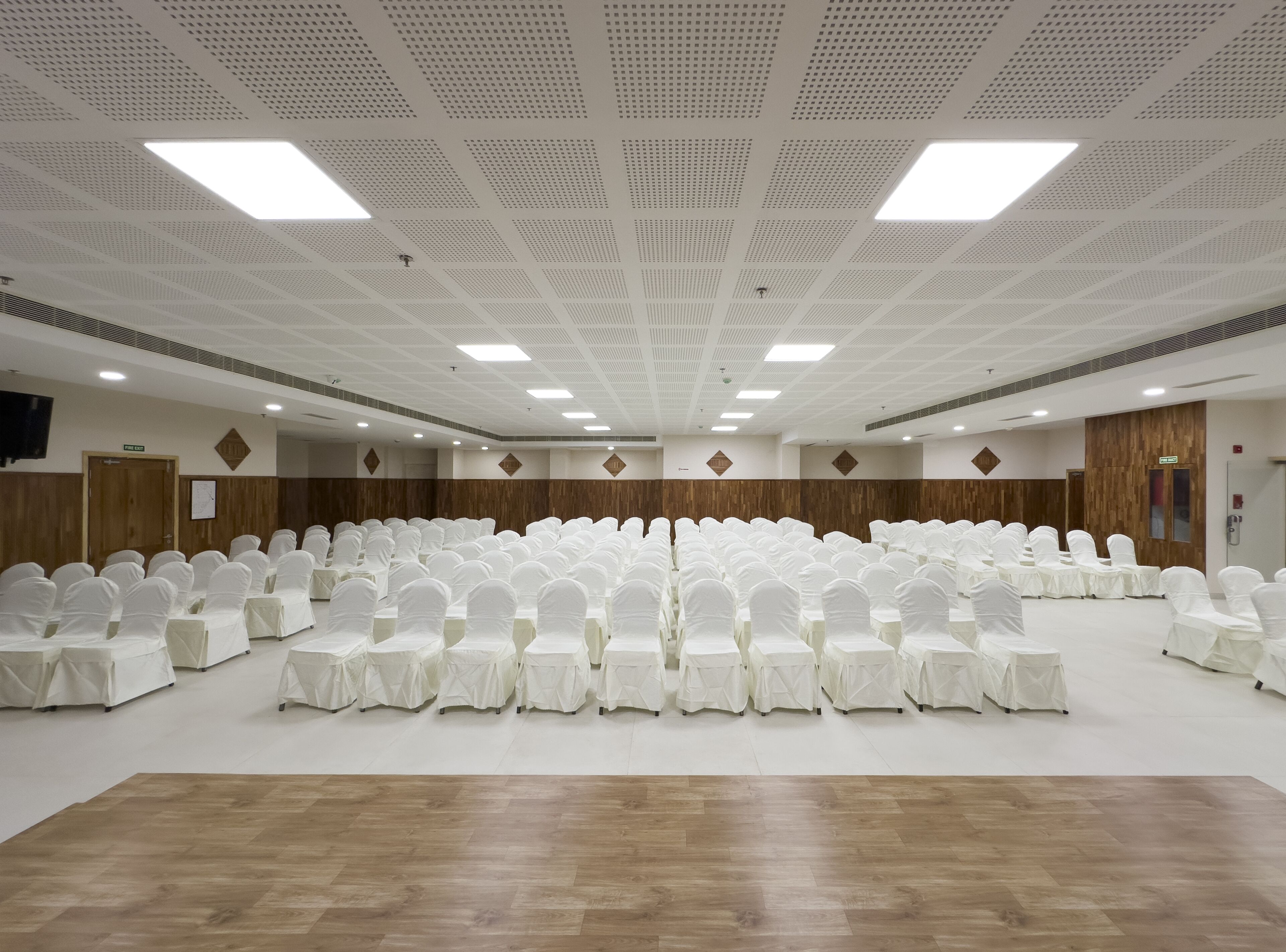 A large conference room with rows of white-covered chairs and tables, wooden paneling on the walls, and a high ceiling with recessed lighting.