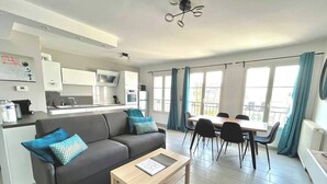 Una sala de estar moderna con sofá, mesa de centro, mesa de comedor y sillas. Se observa una zona de cocina con armarios y un microondas.