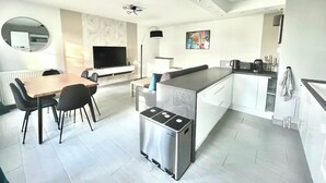 Una cocina moderna con una isla central, un área de comedor con mesa y sillas, y un televisor en la pared.