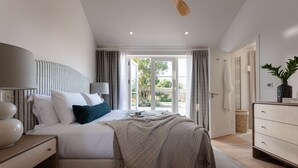 Quarto com cama, mesas de cabeceira, cômoda e vista para o exterior.
