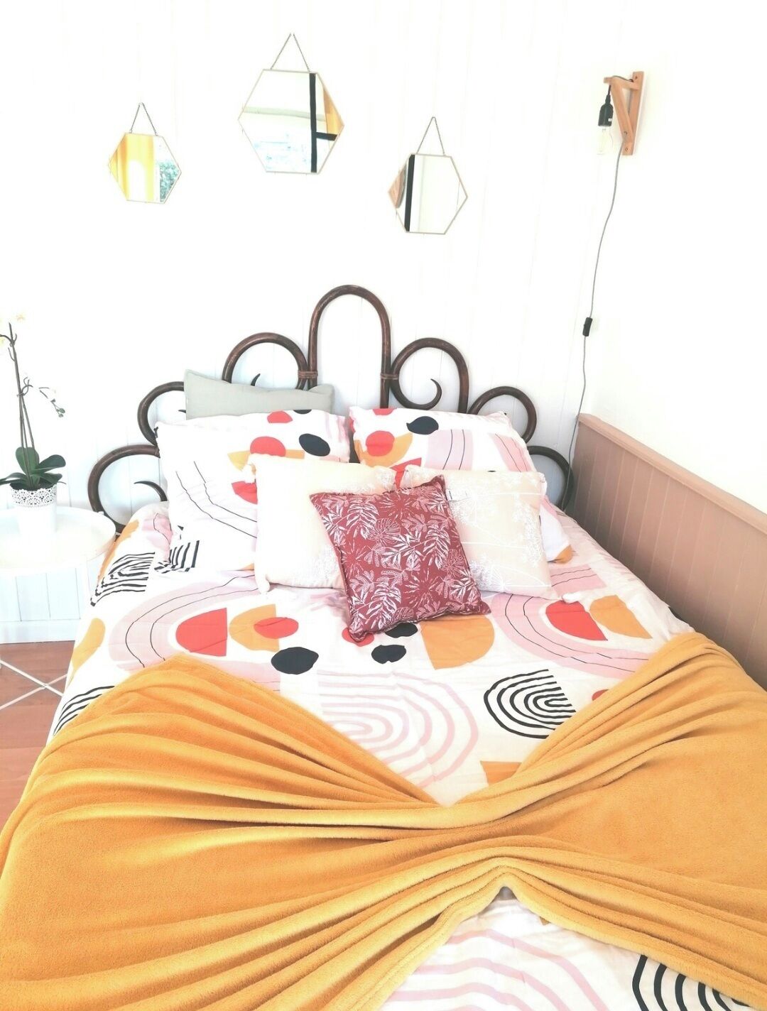 A bed with a patterned bedspread, multiple pillows, and a yellow throw blanket.