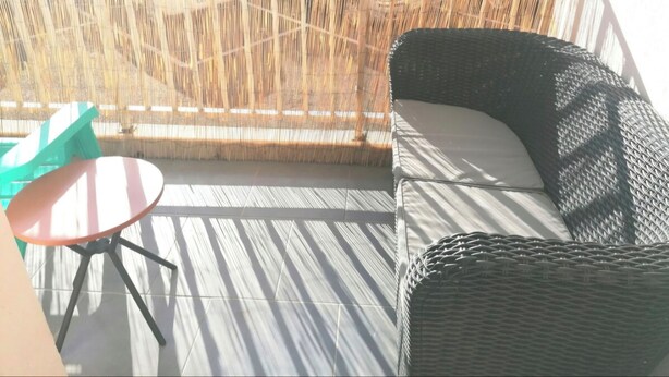 A balcony with wicker furniture, a small round table, and a view of parked cars through a bamboo fence. - Apartment Cosy annemasse (Annemasse)