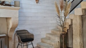 Un interior rústico con un banco de piedra, una silla de mimbre, una planta en maceta y una escalera.