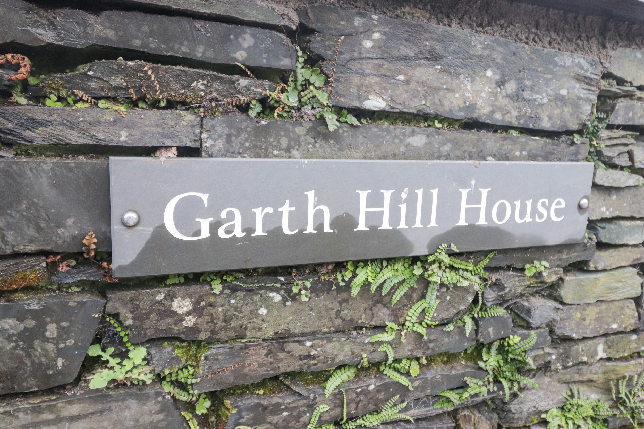 A stone wall with a sign that reads 'Garth Hill House.'